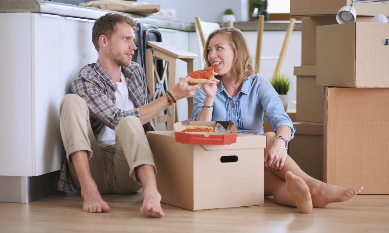 Un couple de primo accédant assis sur le sol qui mange une pizza sur un carton de déménagement