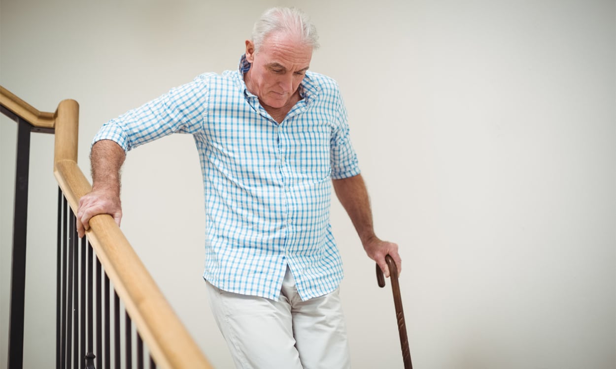 Un homme âgé qui descends des escaliers appuyé sur une canne