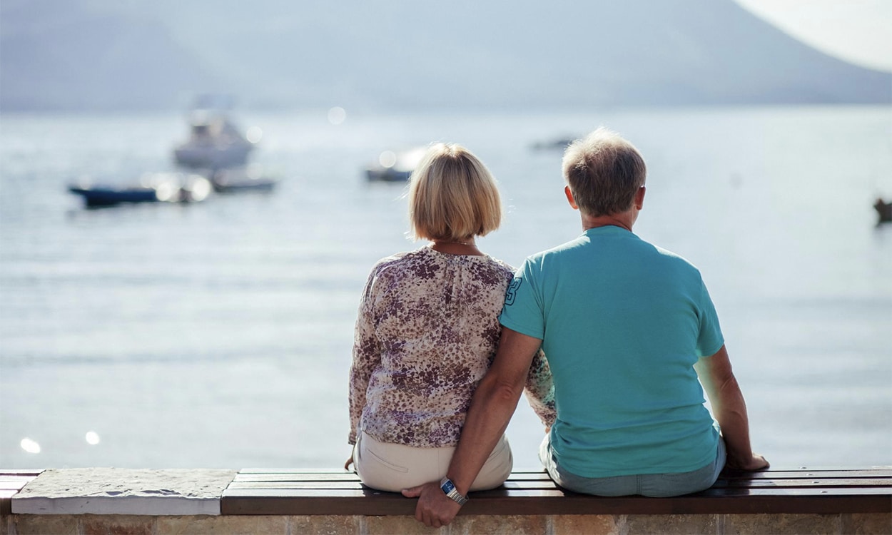 Un couple de retraités de dos assis sur un banc au bord de la mer.