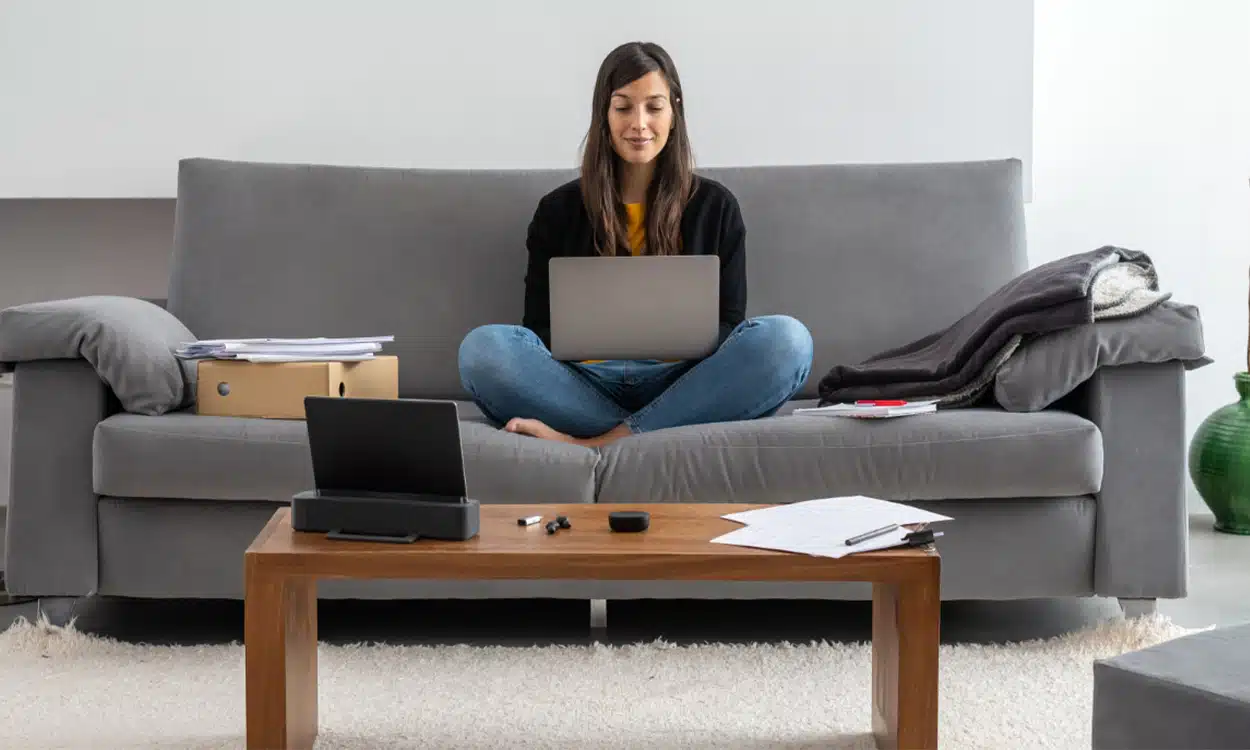 Une jeune femme étudiante qui fait une recherche sur son ordinateur assise dans un canapé