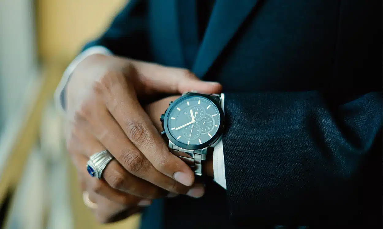Une montre de luxe accrochée au poignet d'un homme tenue par l'autre main.