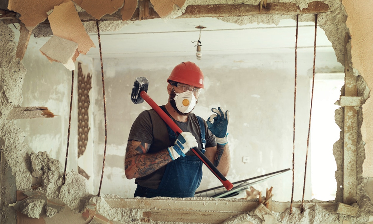 Un ouvrier qui démolit un mur intérieur dans une maison en court de travaux de rénovation énergétique