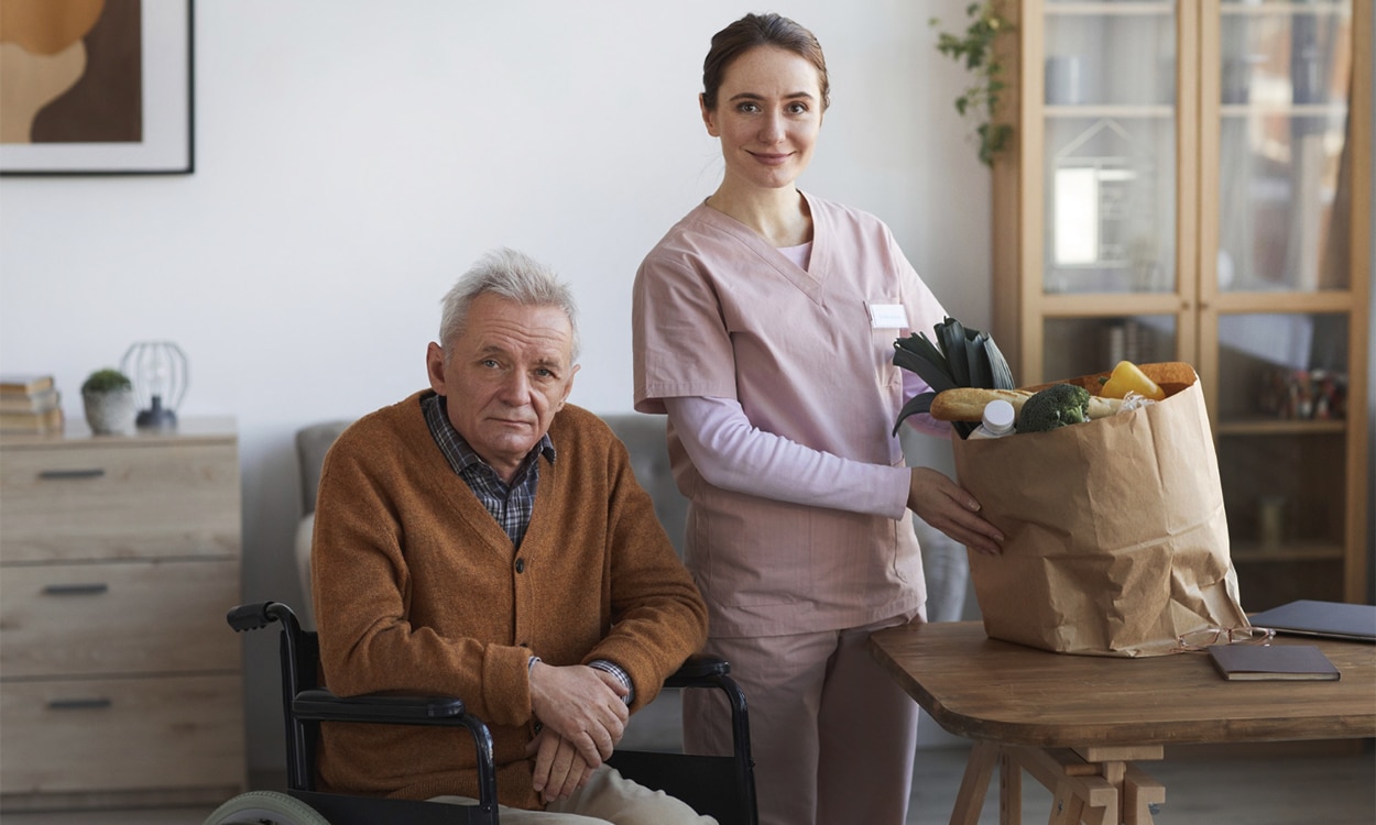 Une aide à domicile qui range les courses d'une homme âgé en fauteuil roulant