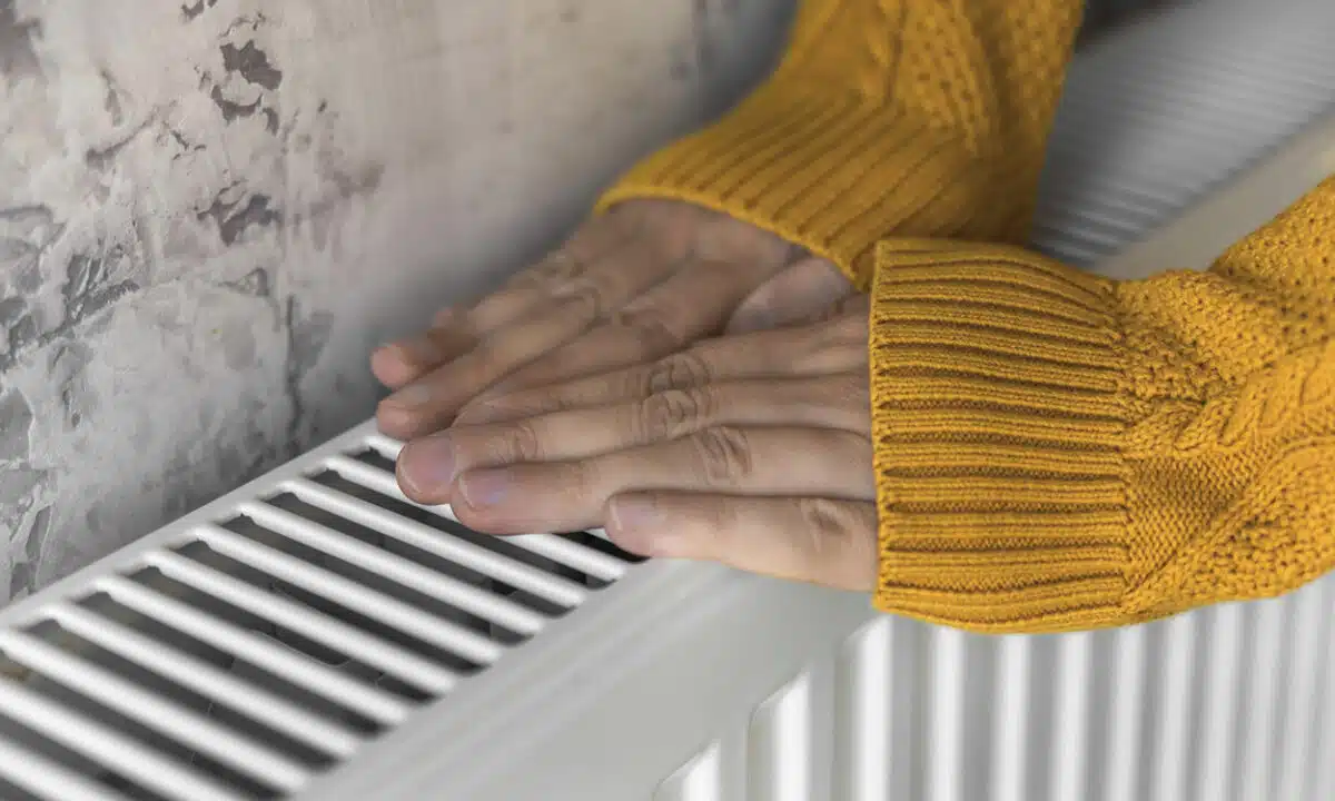 Les mains d'une femme avec un pull orange qui se réchauffent sur un radiateur