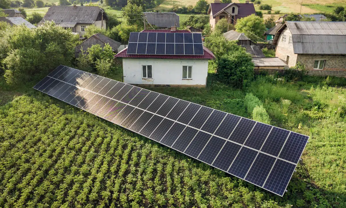 Panneaux solaires installés sur un terrain agricole devant une maison équipée de panneaux photovoltaïques sur son toit