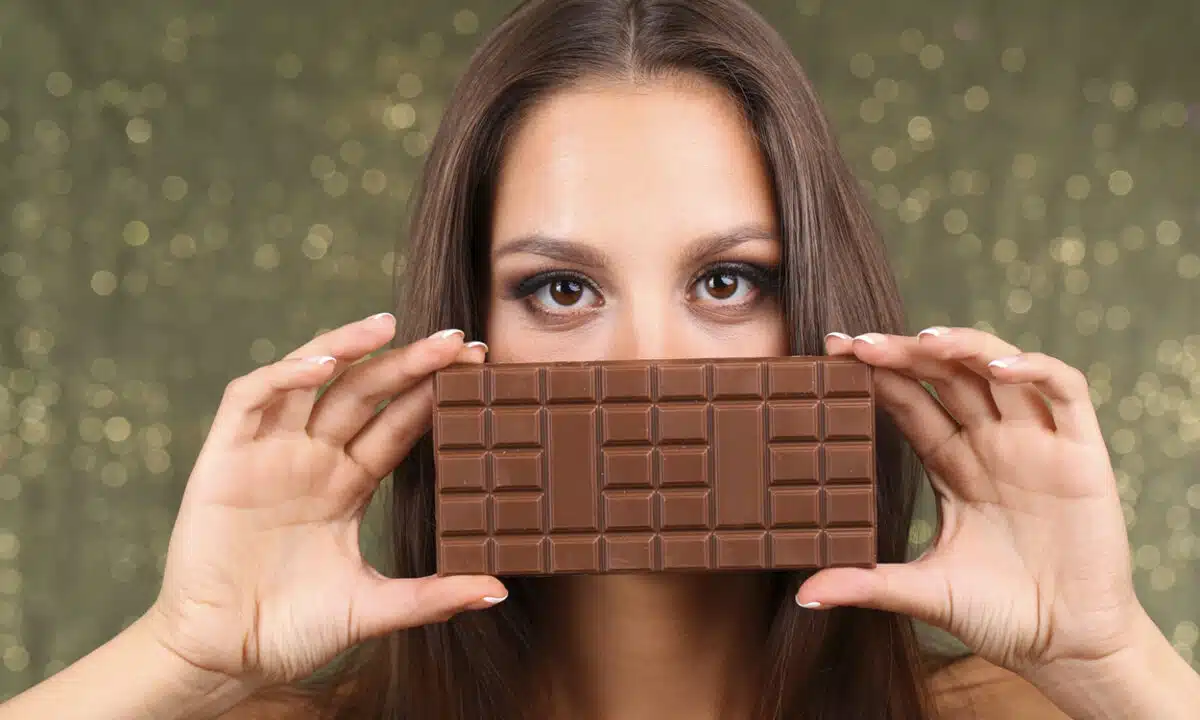 Femme qui tient une tablette de chocolat devant son visage