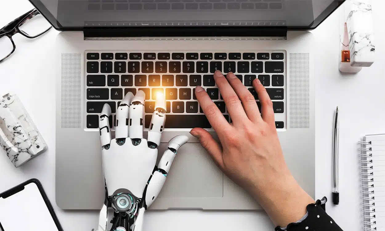 Les mains d'un robot et d'un humain sur un clavier d'ordinateur pour représenter l'intelligence artificielle dans le travail
