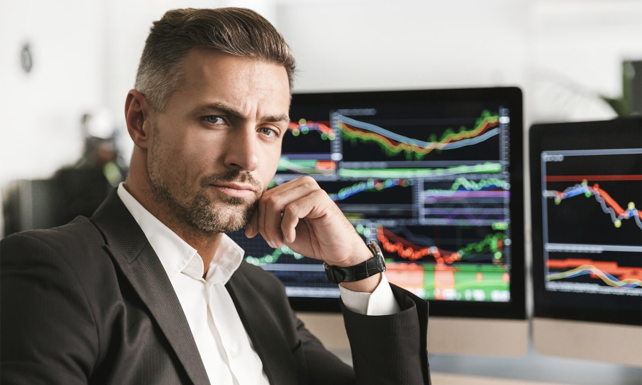 Un trader devant ses écran d'ordinateurs qui affichent des graphiques boursiers
