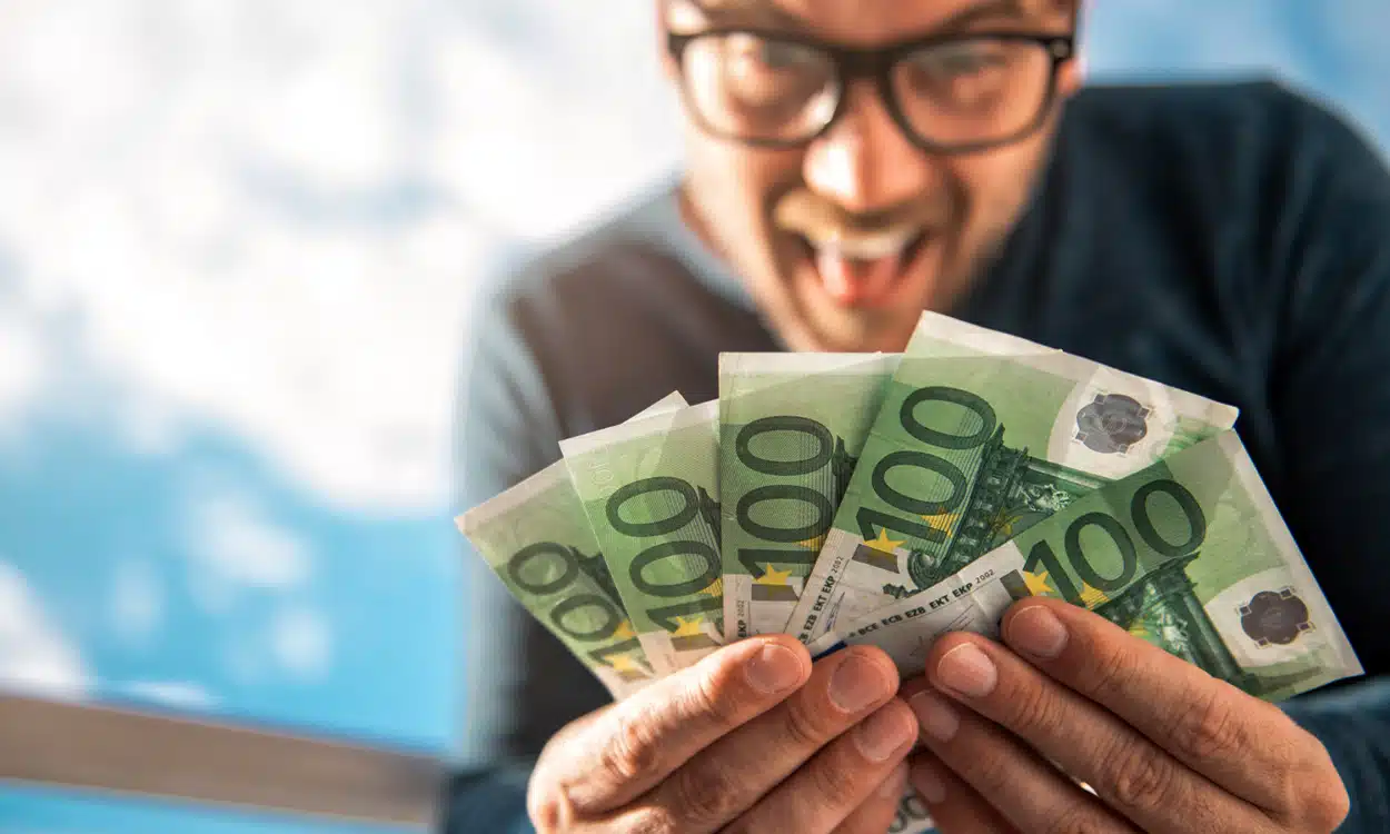 Homme heureux qui tient une liasse de billets de 100 euros