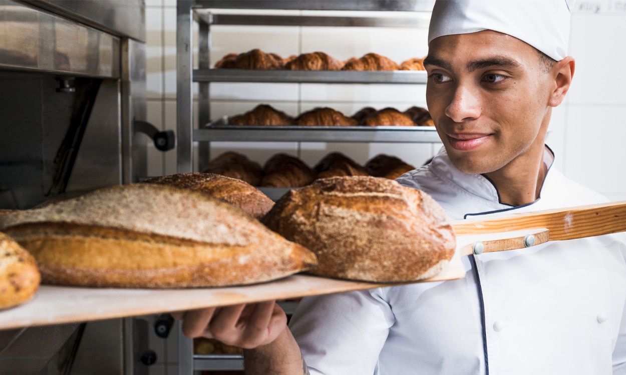 Un apprenti boulanger qui sort sa fournée de pain du four