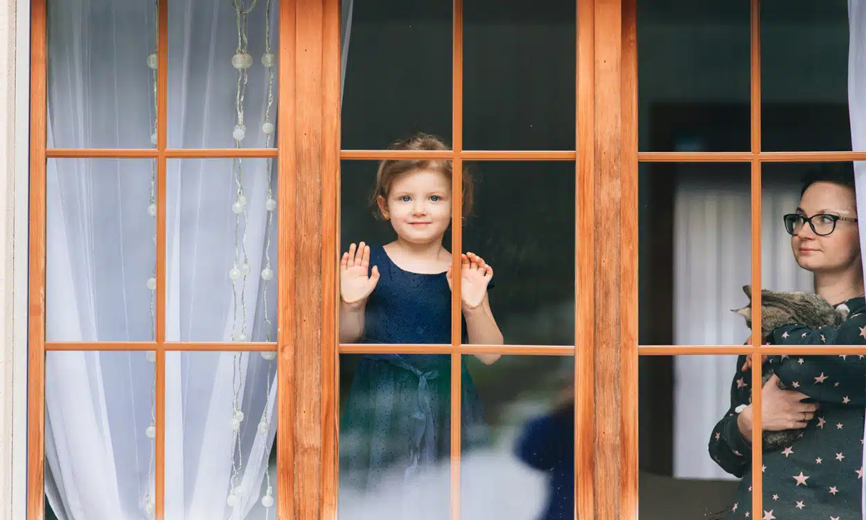 Petite fille souriante derrière une fenêtre en bois avec sa maman
